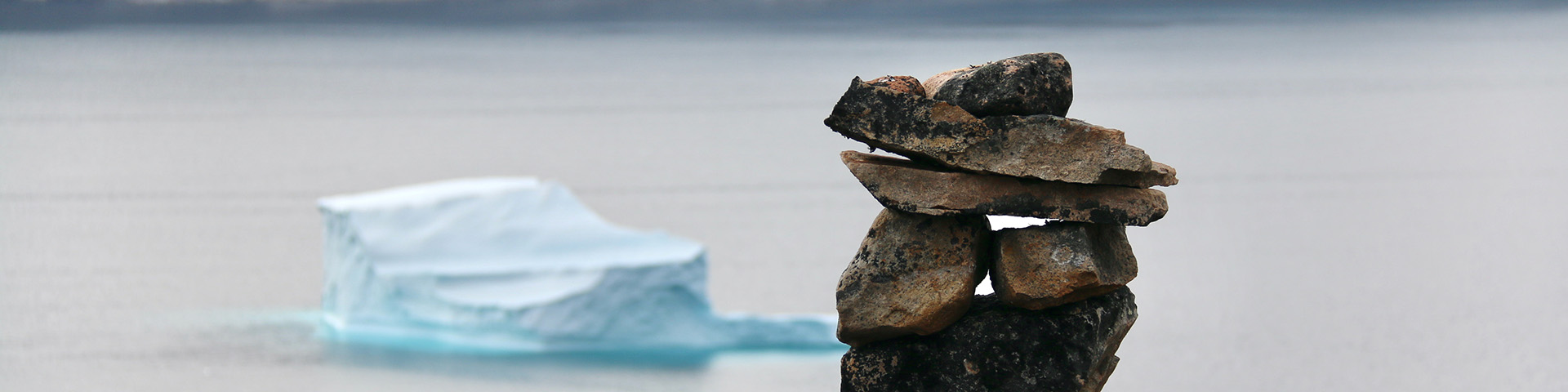 An inuksuk with an iceberg in the background.