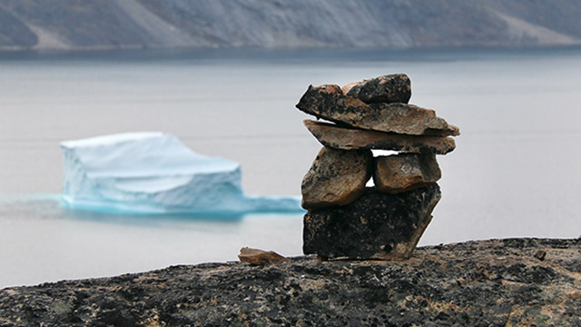 An inuksuk with an iceberg in the background.