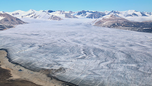 Aerial view of a massive glacier, with mountains in the distance.