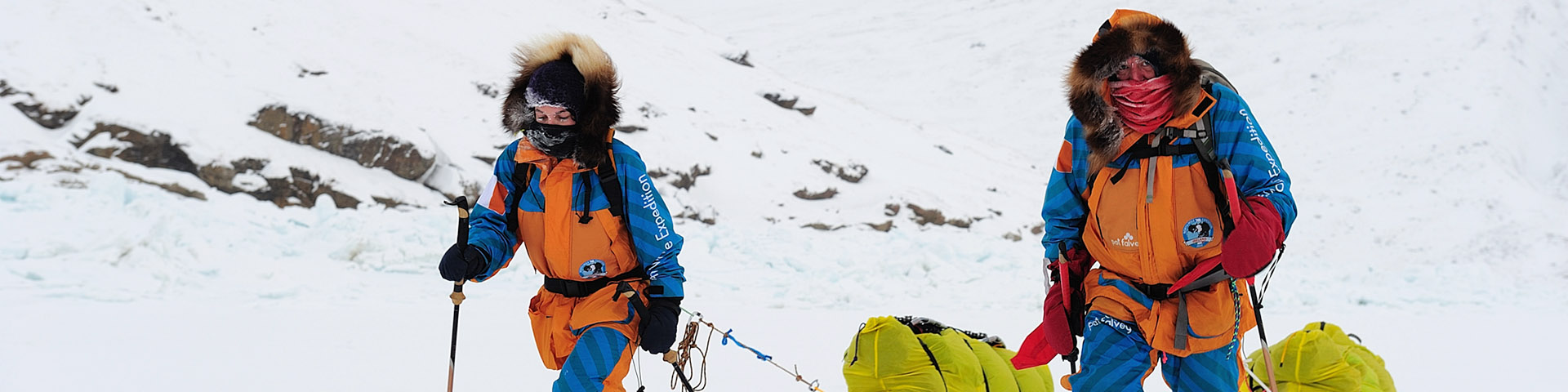 Deux skieurs tirant des luges à travers un paysage enneigé.