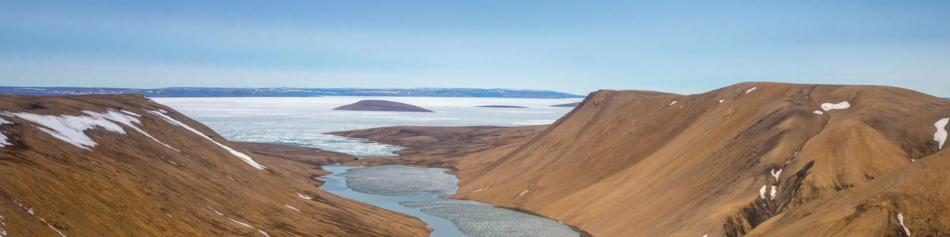 A bird's-eye view of mountains and a large body of water covered with frozen ice.