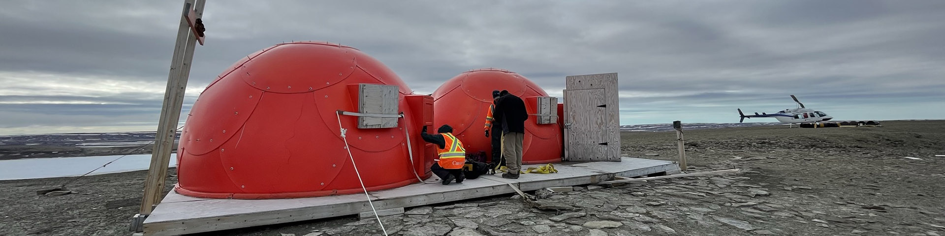 Parks Canada staff members conducting maintenance on two red dome structures in a wide-open landscape.