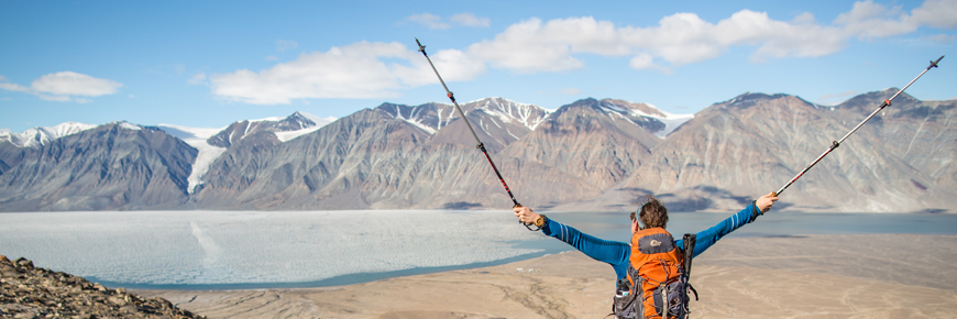 A hiker, arms outstretched, looking at mountains.