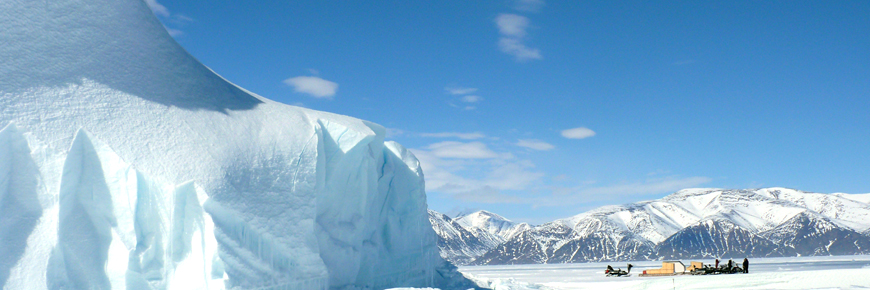 Un groupe de personnes en motoneige à côté d'un énorme iceberg.