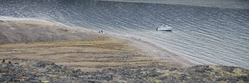 A boat near the shore. Two people are walking on the shoreline.