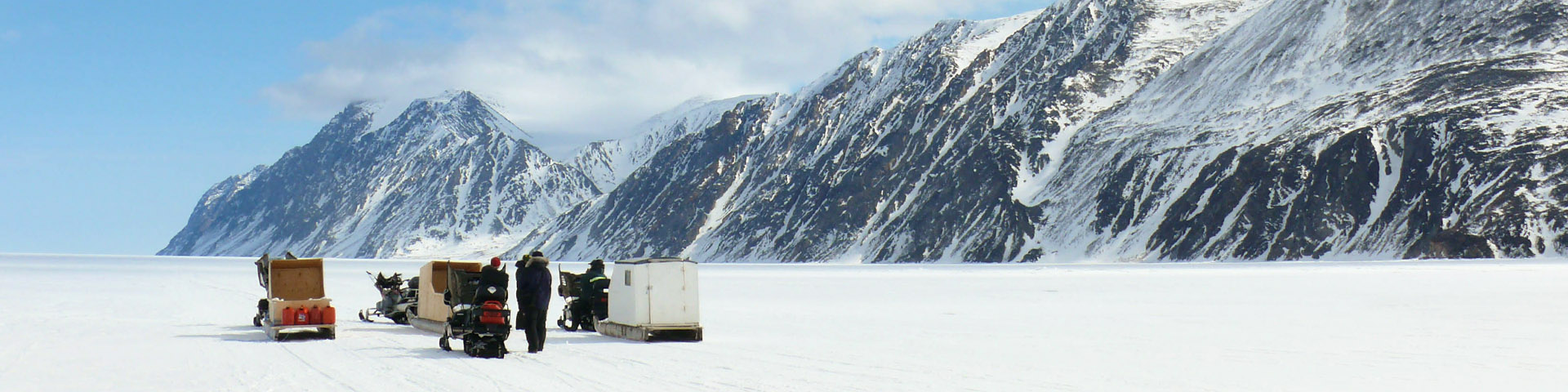 A group of people with skidoos and qamutiks on the ice