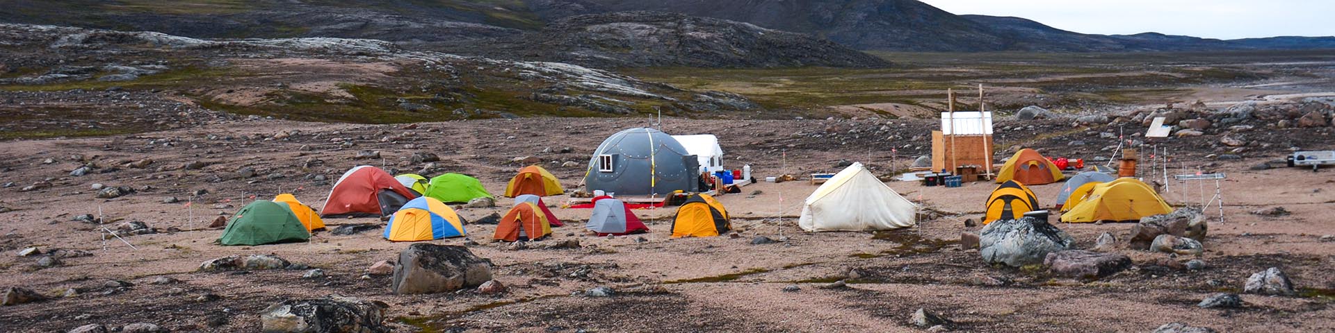 A group of tents and shelters surrounded by tundra scenery. 