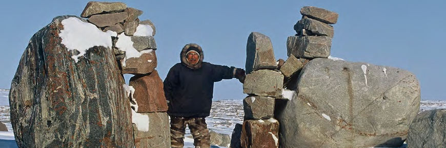 Un homme debout entre deux cairns de roche ou inuksuit.