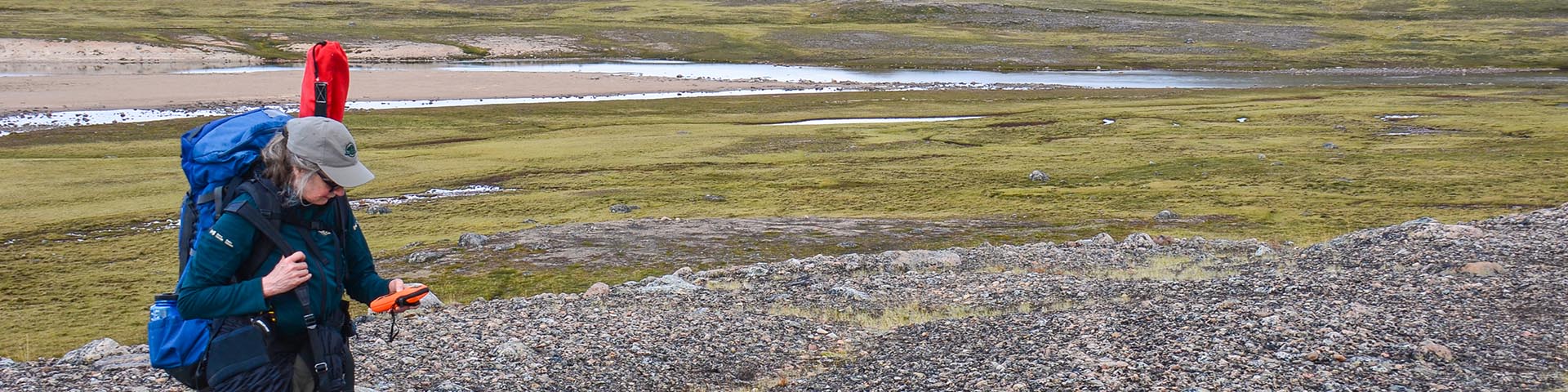 A Parks Canada staff on the tundra holding a communications device 