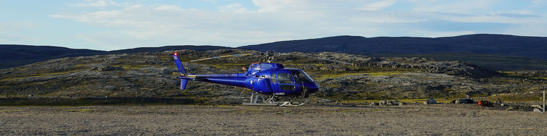 A blue helicopter on a dirt runway surrounded by tundra scenery. 
