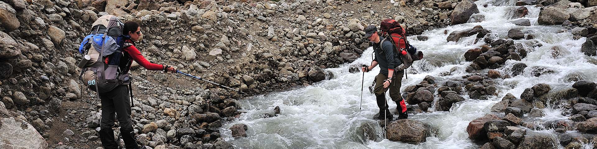 Deux randonneurs traversant un cours d'eau rocailleux et impétueux dans un environnement rocheux. 