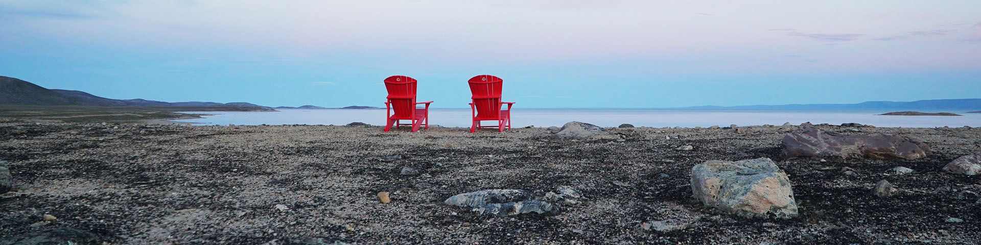 Two red Parks Canada chairs overlooking tundra scenery and Wager Bay. 