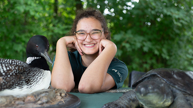 A Parks Canada staff member poses between a model of a loon and turtle
