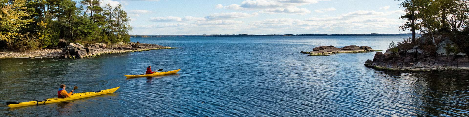 Two people paddle kayaks beside islands.