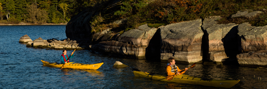 Kayaks pass in front of a rocky shoreline.