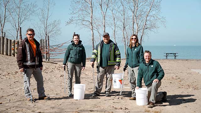 Parks Canada employees and volunteers who pose for a photo with buckets and trash pickers in front of a beach. 