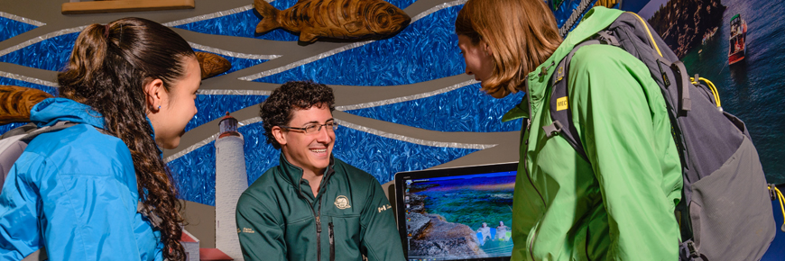 Park staff helps two visitors with a map at the front desk.