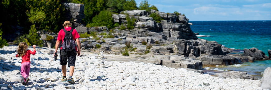 A parent and child hike along the rocky shoreline. 