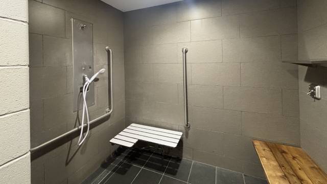 Une douche accessible de plain-pied équipée d’un banc rabattable, de barres d’appui et d’une douchette à main.