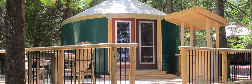 A yurt in the forest with chairs on the deck.