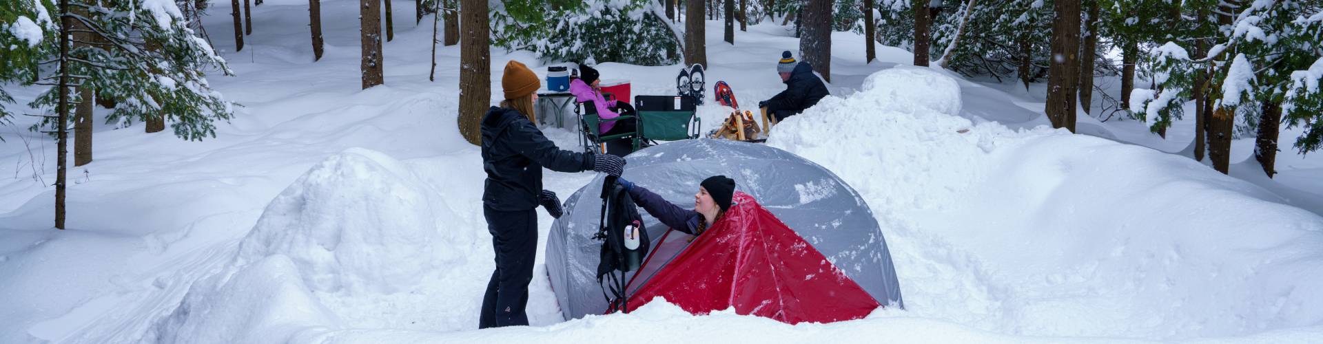 Campers setting up a tent at a snowy forest campsite.