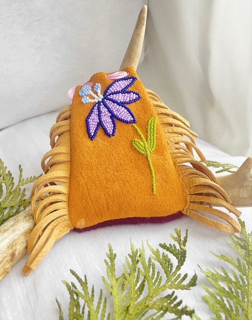 Orange handmade pouch with a purple flower displayed against a soft fabric background