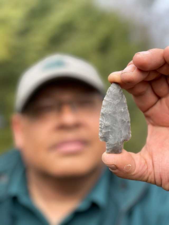 A person holds up a small gray stone arrowhead