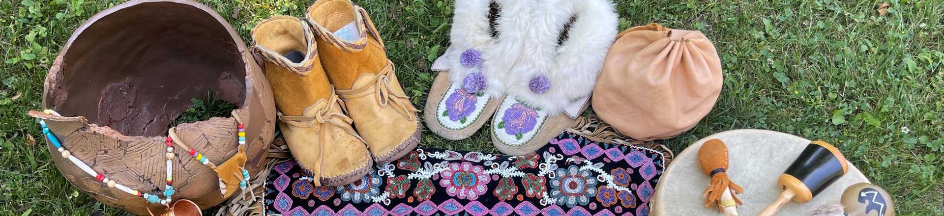 Articles autochtones, notamment des mocassins, des pièces de perles, un tambour, des plumes et un petit panier.