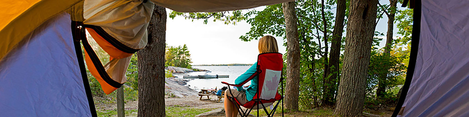 A camper sitting on a chair outside a tent on the shoreline. 