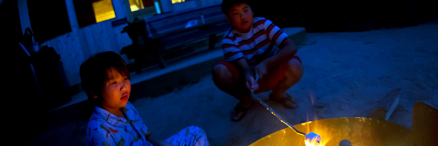 Two kids roast marshmallows outside their cabin. 