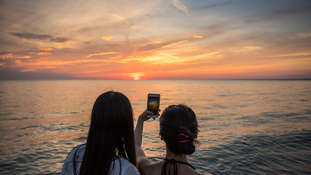 Deux personnes prennent une photo d'un coucher de soleil.