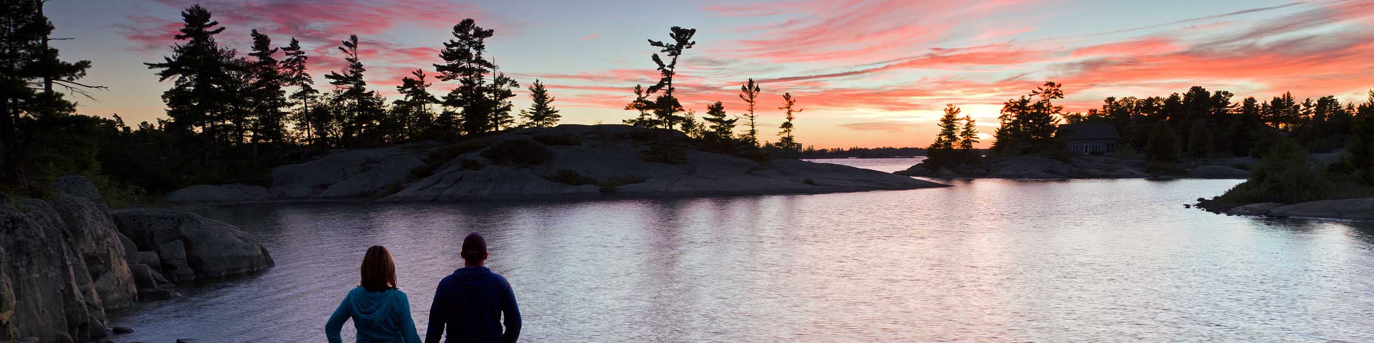 Two visitors watch a sunset over the water.