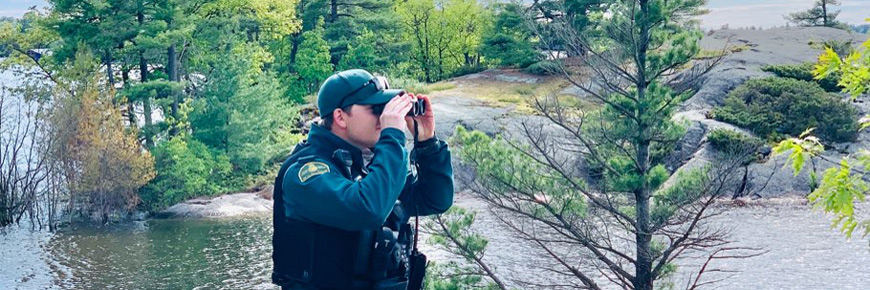 A park warden uses binoculars to look over the water
