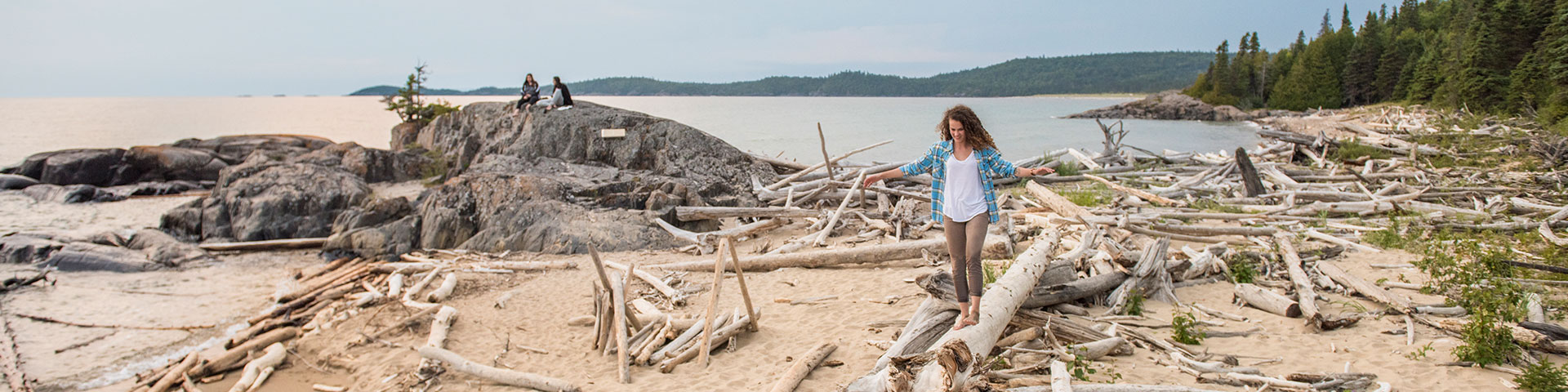 A woman balancing on driftwood on the beach.