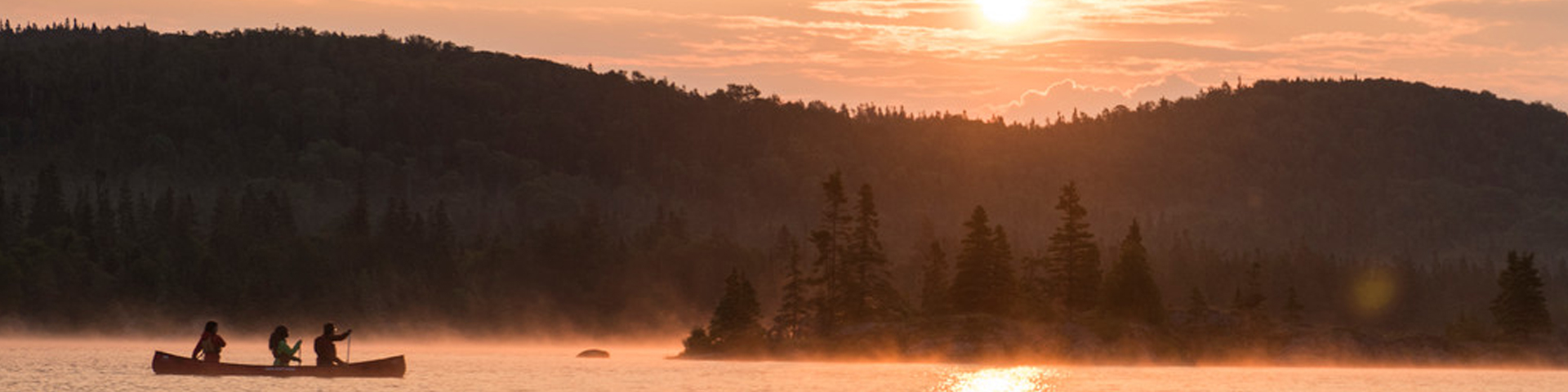 Un groupe pagaye en canoë au coucher du soleil.