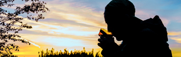 A person drinking coffee outdoors at sunset.