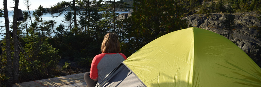 A person sitting beside a tent in overlooking a lake.
