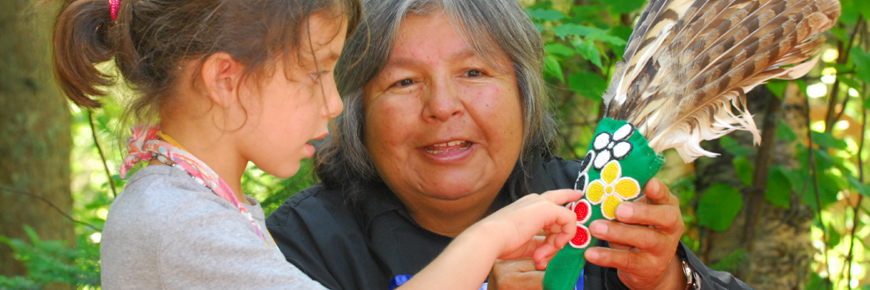 A woman showing a young girl an eagle feather fan.