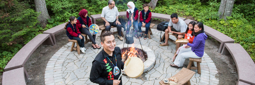 A person with a hand drum standing in front of an outdoor fireplace.