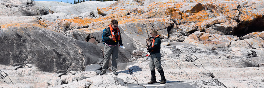 Two people standing on a rocky shoreline.