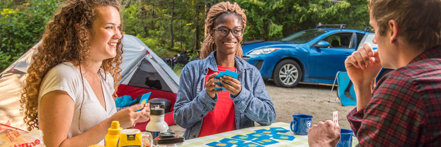 Three people playing cards at a picnic table.