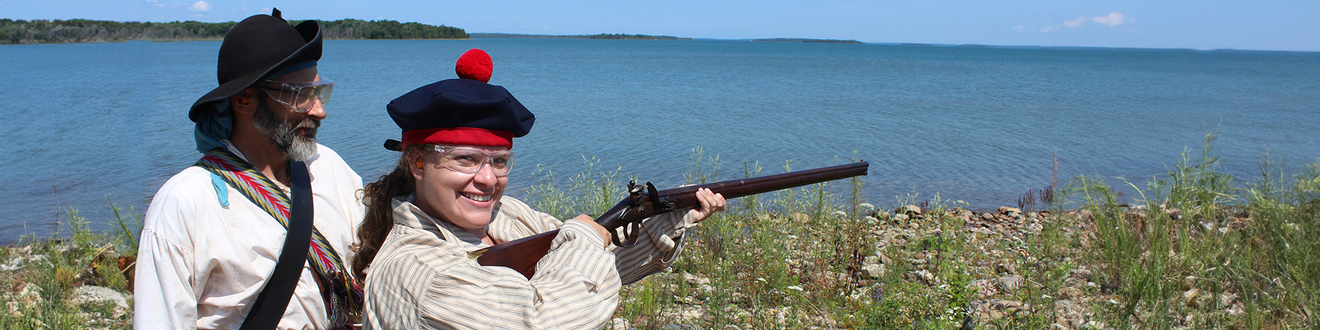 A visitor poses with the flintlock trade musket and costumed supervisor.