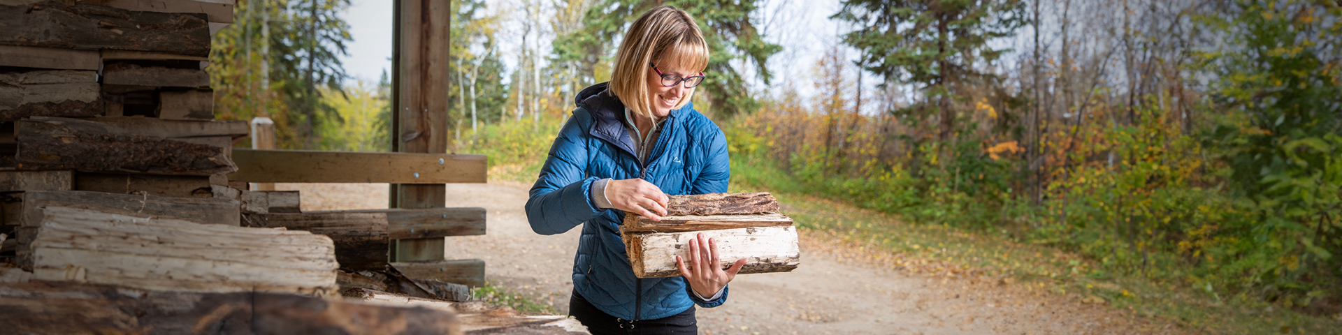 A woman gathers an armload of firewood from a pile
