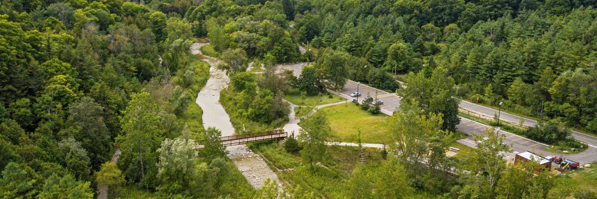 Vue aérienne d'une forêt verdoyante avec une rivière sinueuse, un petit pont et les zones de stationnement.