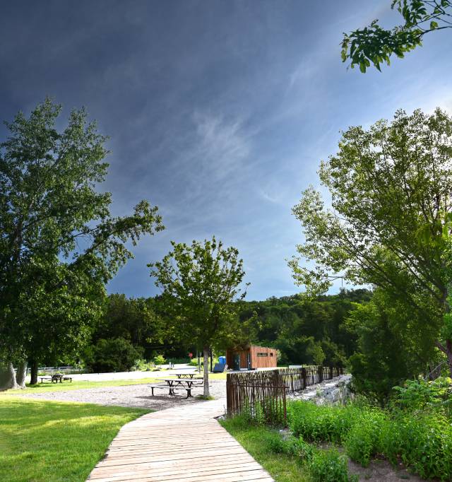 A scenic view of a park featuring a wooden pathway leading to picnic tables and a small building.