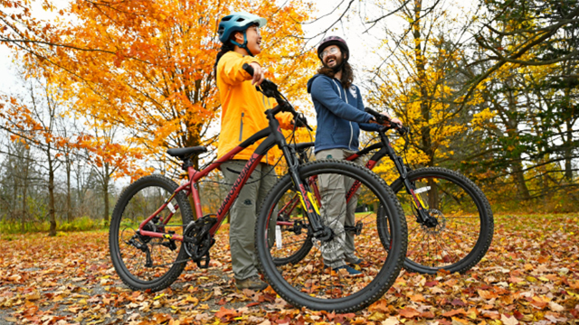 Two adults on mountain bikes surrounded by yellow, orange, and red leaves. 