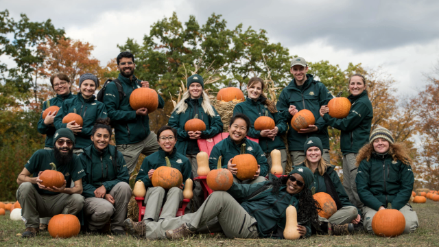 Parks Canada staff posing with pumpkins outdoors in front of fall foliage.