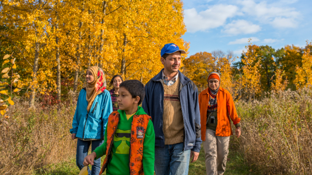 A family of five walking along a forest path surrounded by fall colours at Rouge National Urban Park.