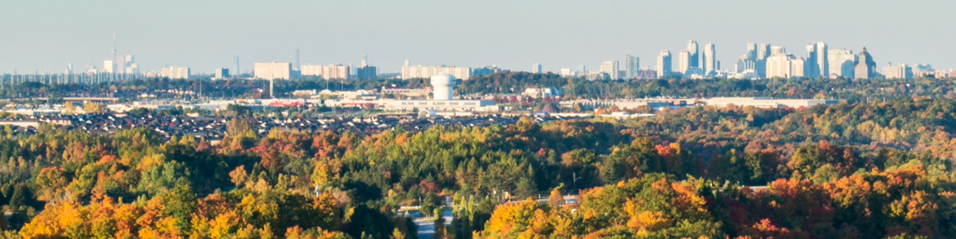 Vue panoramique du parc urbain national de la Rouge avec un feuillage d'automne éclatant en vert, jaune, orange et rouge, et la silhouette de la ville au loin.