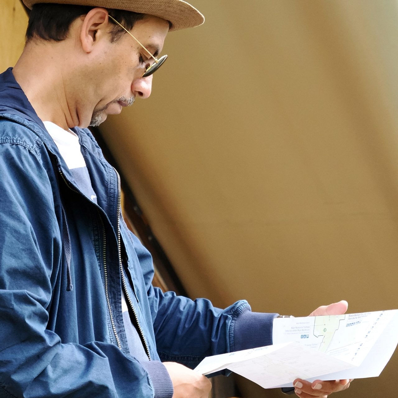 A person in a blue jacket and beige hat holds and looks at a map of Rouge National Urban Park. The roof of a beige tent is visible in the background.